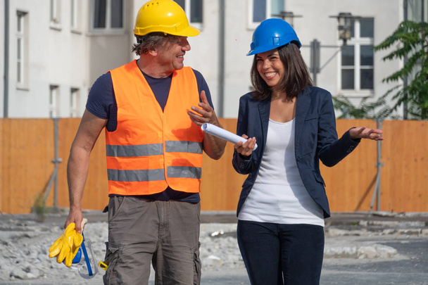 Dwóch inżynierów cywilnych, mężczyzna i brunetka młoda kobieta, rozmawiając i śmiejąc się podczas przerwy w pracy. Zewnątrz - Zdjęcie, obraz