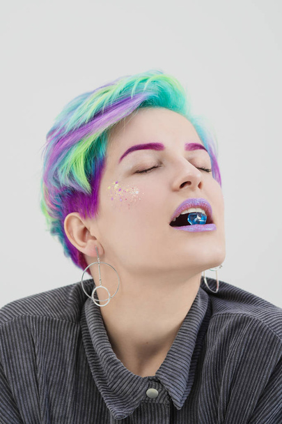 A young woman with short pixie bob haircut and dyed hair, holds in the mouth and in the hands gemstones and jewels. - Foto, Imagen