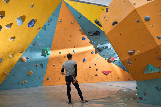 Boulderer with physical disability looking thoughtfully at colourful artificial walls - 写真・画像