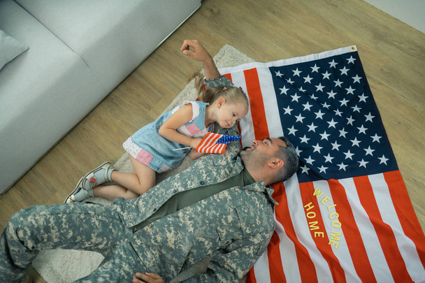 Military servant lying on the floor near his cute lovely daughter - Foto, afbeelding