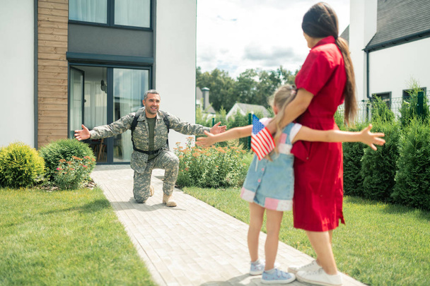 Military man standing on his knee while seeing wife and daughter - Фото, зображення