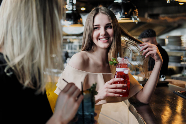 Kaksi nuorta fiksua, kaunista tyttöä mekoissa istuu baarissa. Juo punaisia ja sinisiä cocktaileja laseista tubuleilla
. - Valokuva, kuva