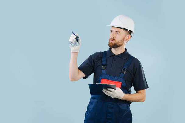 Construction engineer in a white helmet and blue uniform with a paper schematics - Fotoğraf, Görsel