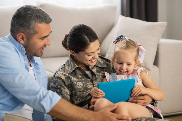 Militar mulher assistindo desenhos animados com filha e marido
 - Foto, Imagem