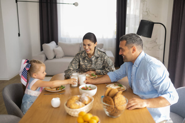 Military woman smiling broadly while having breakfast with family - Foto, Imagen