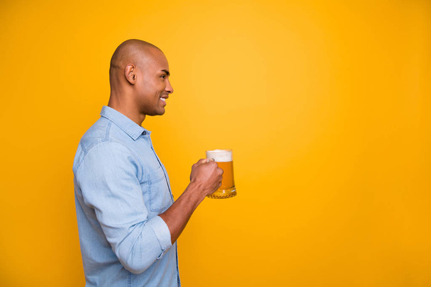Profiili kuva tumma iho viileä hämmästyttävä kaveri pitää käsissä olut lasi avulla juhlia kulumista farkut denim paita eristetty keltainen tausta
 - Valokuva, kuva