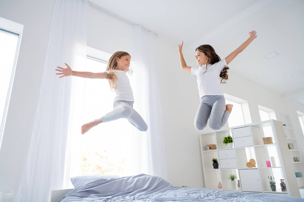 Low angle photo of cheerful lovely children blonde brunette hairstyle jump indoors bed raise hands feel cheerful room - Foto, immagini