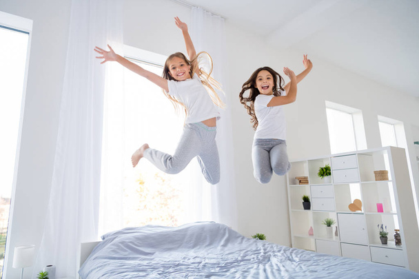 Low angle photo of cheerful kids jumping bed have free time raise hands feel content room indoors apartment - Fotoğraf, Görsel