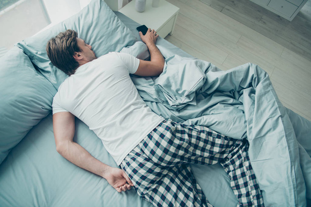 Top high angle photo of peaceful youth lying on bed holding smart cell phone wearing white t-shirt checkered plaid shorts in room indoors - Valokuva, kuva