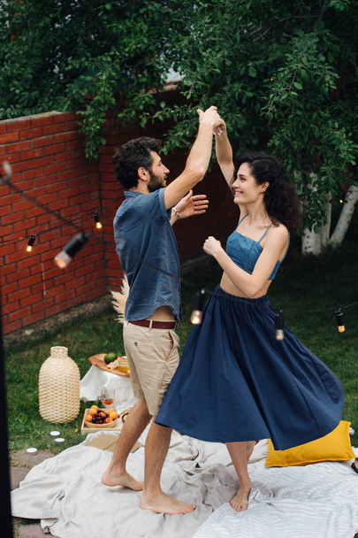 Couple in love is slow-dancing together during picnic on lawn in their courtyard - Fotoğraf, Görsel