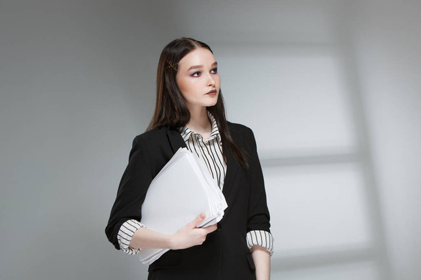 Young beautiful female fashion model in a business stylish suit on a rerom background. Holds a stack of papers and a pen. - Фото, изображение