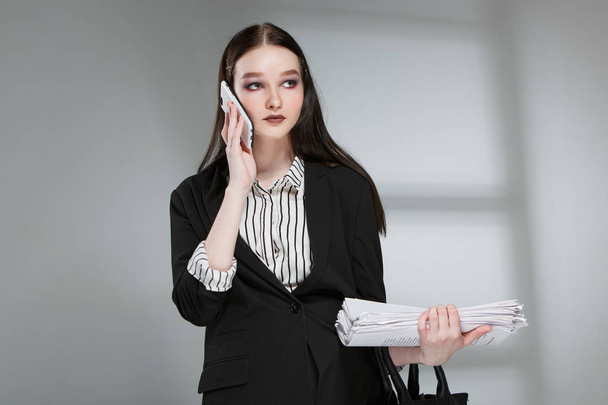 Young beautiful female fashion model in a business stylish suit on a rerom background. Holds a stack of papers and a pen. - Foto, imagen