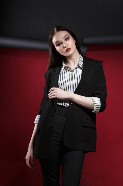 Young beautiful female fashion model in a business stylish suit on a red and black background. - Fotografie, Obrázek