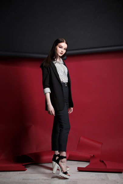 Young beautiful female fashion model in a business stylish suit on a red and black background. - Foto, Imagen