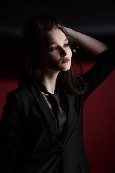 Young beautiful female fashion model in a business stylish suit on a red and black background. - Fotó, kép