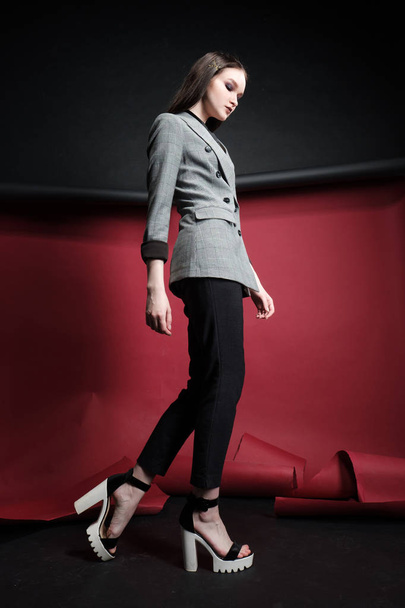 Young beautiful female fashion model in a business stylish suit on a red and black background. - Photo, image