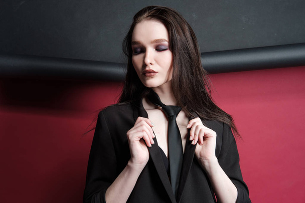 Young beautiful female fashion model in a business stylish suit on a red and black background. - 写真・画像