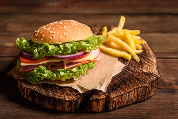 leckere hausgemachte Burger vom Grill mit Rindfleisch, Tomaten, Käse, Gurken und Salat. leckere gegrillte Burger. Craft Beef Burger und Pommes auf Holztisch - Foto, Bild