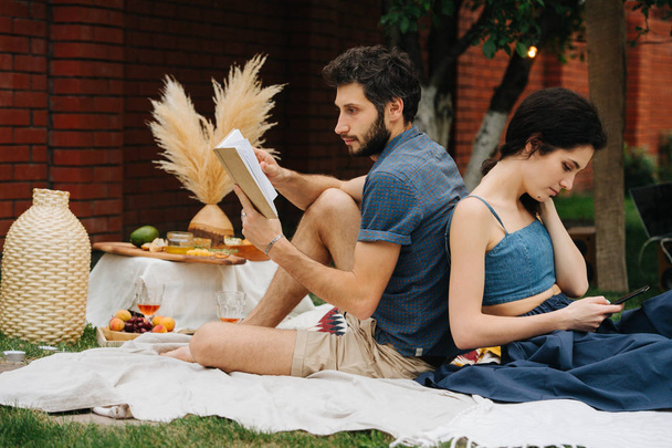 Couple in love, leaning at each other's backs during picnic on lawn in courtyard - Zdjęcie, obraz