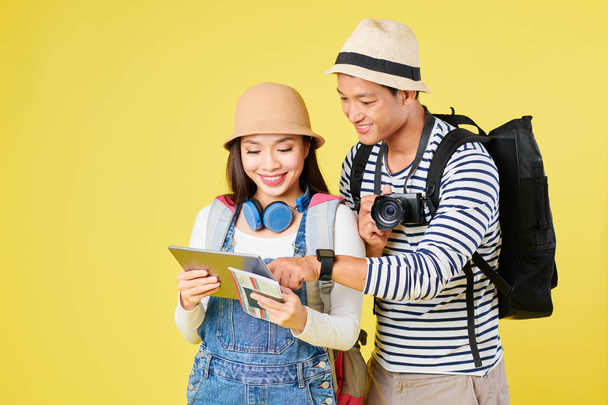 Молодая, улыбающаяся вьетнамская пара, глядя на экран планшетного компьютера и выбирая страну, куда летать в отпуск
 - Фото, изображение