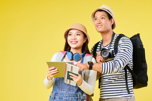 Tablet bilgisayar, sırt çantası ve dijital kamera önlerine bakarak heyecanlı genç Asyalı gezginler - Fotoğraf, Görsel