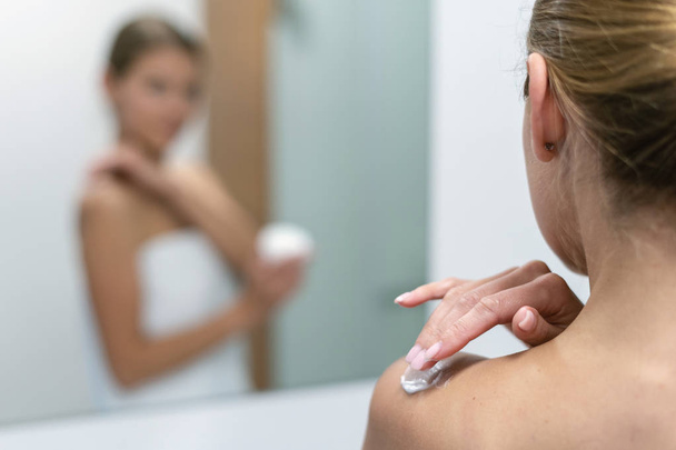 Frau trägt Körpercreme auf Schulter im Badezimmer auf - Foto, Bild