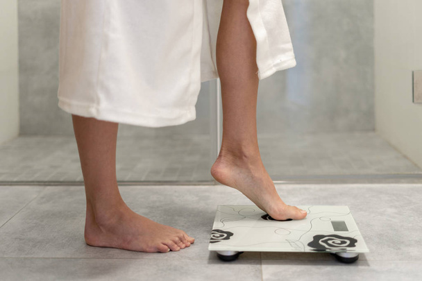 Woman in white bathrobe standing on weigher - Photo, Image