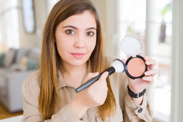 Belle jeune femme utilisant maquillage cosmétique appliquer de la poudre avec une expression confiante sur le visage intelligent pensée grave
 - Photo, image