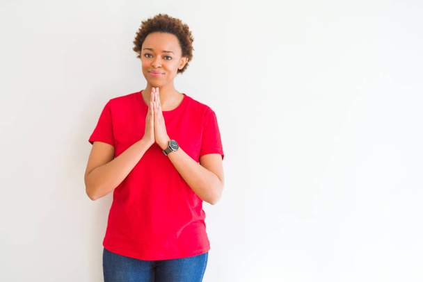 Giovane bella donna afro-americana su sfondo bianco pregando con le mani insieme chiedendo perdono sorridente fiducioso
. - Foto, immagini