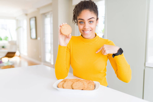Молодий афроамериканець дівчина їсть здорове ціле печиво зерно з сюрпризом особи вказуючи пальцем до себе - Фото, зображення