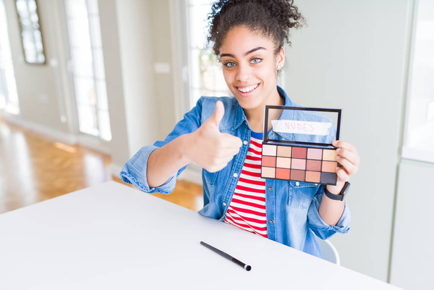 Young african american woman holding shadows cosmetics palette happy with big smile doing ok sign, thumb up with fingers, excellent sign - Φωτογραφία, εικόνα