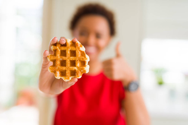 Joven afroamericana americana comiendo dulce waffle feliz con gran sonrisa haciendo ok signo, pulgar hacia arriba con los dedos, excelente signo
 - Foto, Imagen