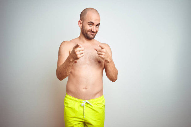 Fiatal félmeztelen ember nyaralni viselt sárga fürdőruhák több mint elszigetelt háttér rámutatva ujjak a kamera boldog és vicces arc. Jó energia és vibrafon. - Fotó, kép