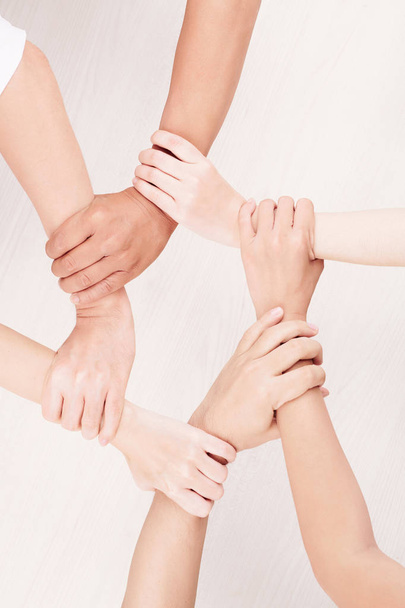 Крупный план группы молодых людей, держащихся за руки и создающих цепь из рук на белом фоне
 - Фото, изображение