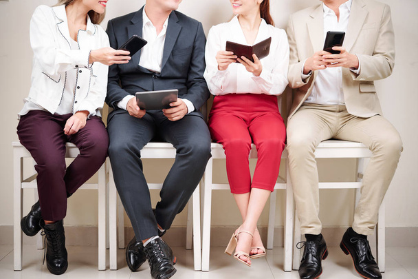 Close-up of young businessmen and businesswomen sitting on chairs and using their gadgets tablet pc and mobile phone - Foto, imagen