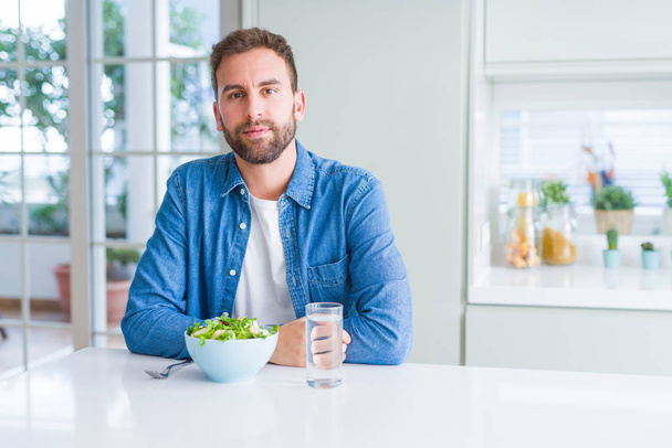 Όμορφος άνθρωπος που τρώει φρέσκια υγιεινή σαλάτα με σοβαρή έκφραση στο πρόσωπο. Απλό και φυσικό κοιτάζοντας την κάμερα. - Φωτογραφία, εικόνα