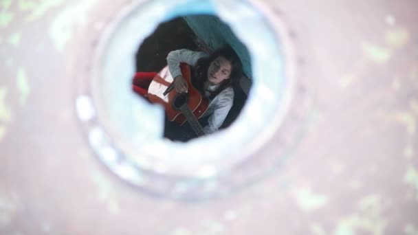Een jonge vrouw zit en speelt gitaar in het oude verlaten schip. Zicht door het schip Patrijspoort. - Video