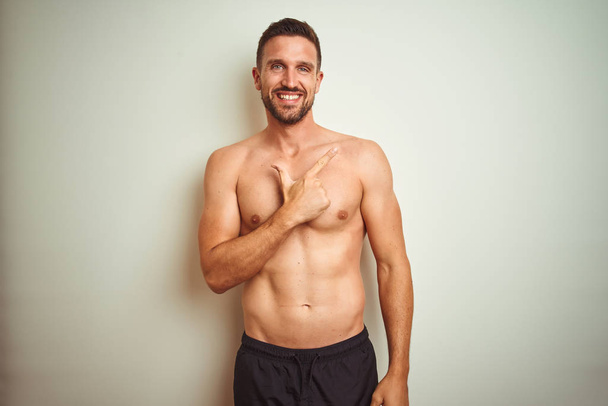 Young handsome shirtless man over isolated background cheerful with a smile of face pointing with hand and finger up to the side with happy and natural expression on face - Photo, Image