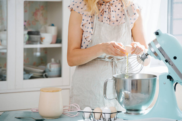 young woman breaks an egg into the bowl of food processor to make a dough  - Photo, Image