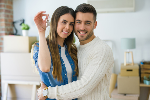 Genç çift yeni bir eve hareket, yeni dairenin anahtarlarını gösteren aşk sarılmak çok mutlu gülümseyen - Fotoğraf, Görsel