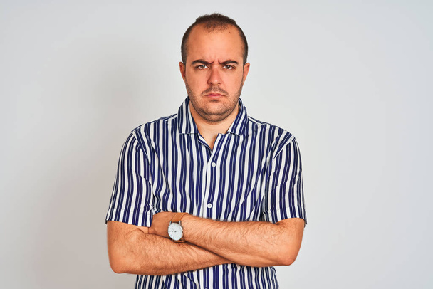 Fiatal férfi viselt kék csíkos inget állva elszigetelt fehér háttér szkeptikus és ideges, disjóváhagyásáról kifejezés arcon a keresztezett fegyverek. Negativ személy. - Fotó, kép