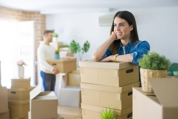 Young couple moving to a new home, beautiful woman smiling leaning on cardboard boxes - Photo, Image