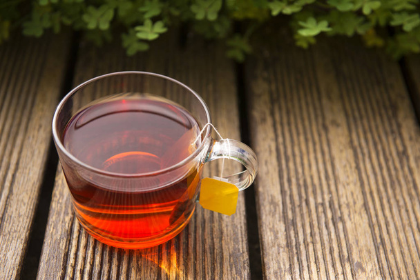 Γυαλί διαφανές φλιτζάνι μαύρο τσάι και ξηρό τσάι σε σακούλες στο παλιό ξύλινο φόντο. - Φωτογραφία, εικόνα