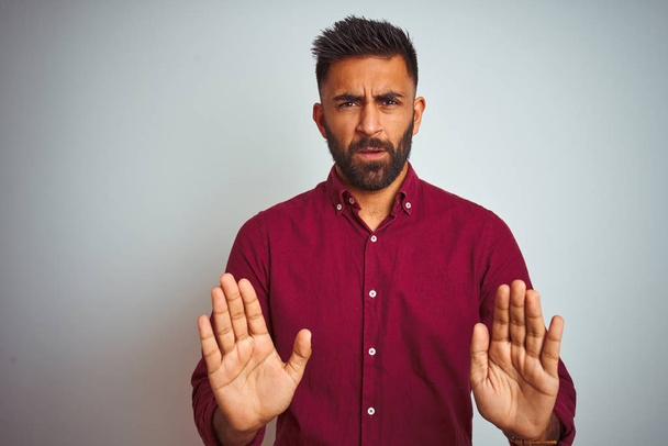Young indian man wearing red elegant shirt standing over isolated grey background Moving away hands palms showing refusal and denial with afraid and disgusting expression. Stop and forbidden. - Valokuva, kuva
