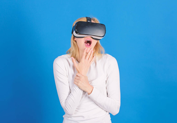 Woman wearing virtual reality goggles in blue background. Woman enjoying cyber fun experience in vr. Amazed young woman touching the air during the VR experience. Technical network. - Foto, afbeelding