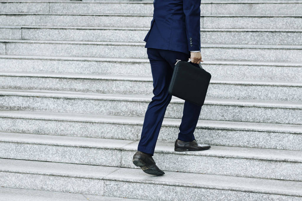 Cropped image of businessman with briefcase walking up the stairs outdoors - Fotoğraf, Görsel