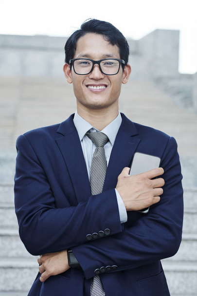 Portret van jonge zelfverzekerde succesvolle Vietnamese ondernemer met smartphone in de hand kijken naar camera - Foto, afbeelding