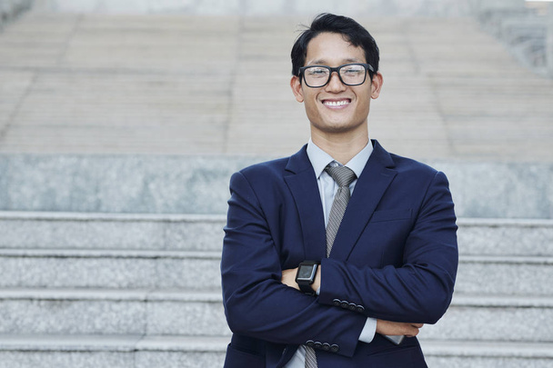 Portrait of young successful Asian businessman in glasses folding arms and looking at camera - Photo, Image