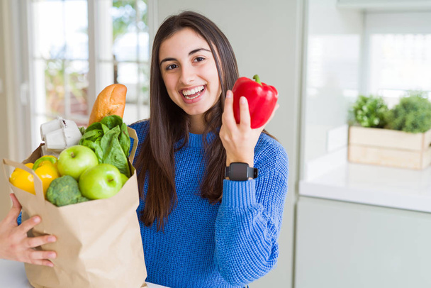 Young beautiful woman smiling holding a paper bag full of grocer - Foto, Imagen
