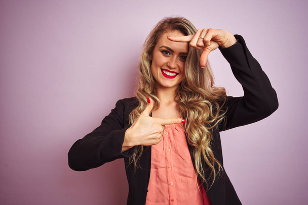 Young beautiful business woman wearing elegant jacket standing over pink isolated background smiling making frame with hands and fingers with happy face. Creativity and photography concept. - Foto, imagen
